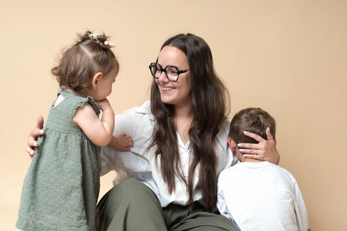 Sarah sourit à sa fille, ses deux enfants contre elle, le garçon de dos