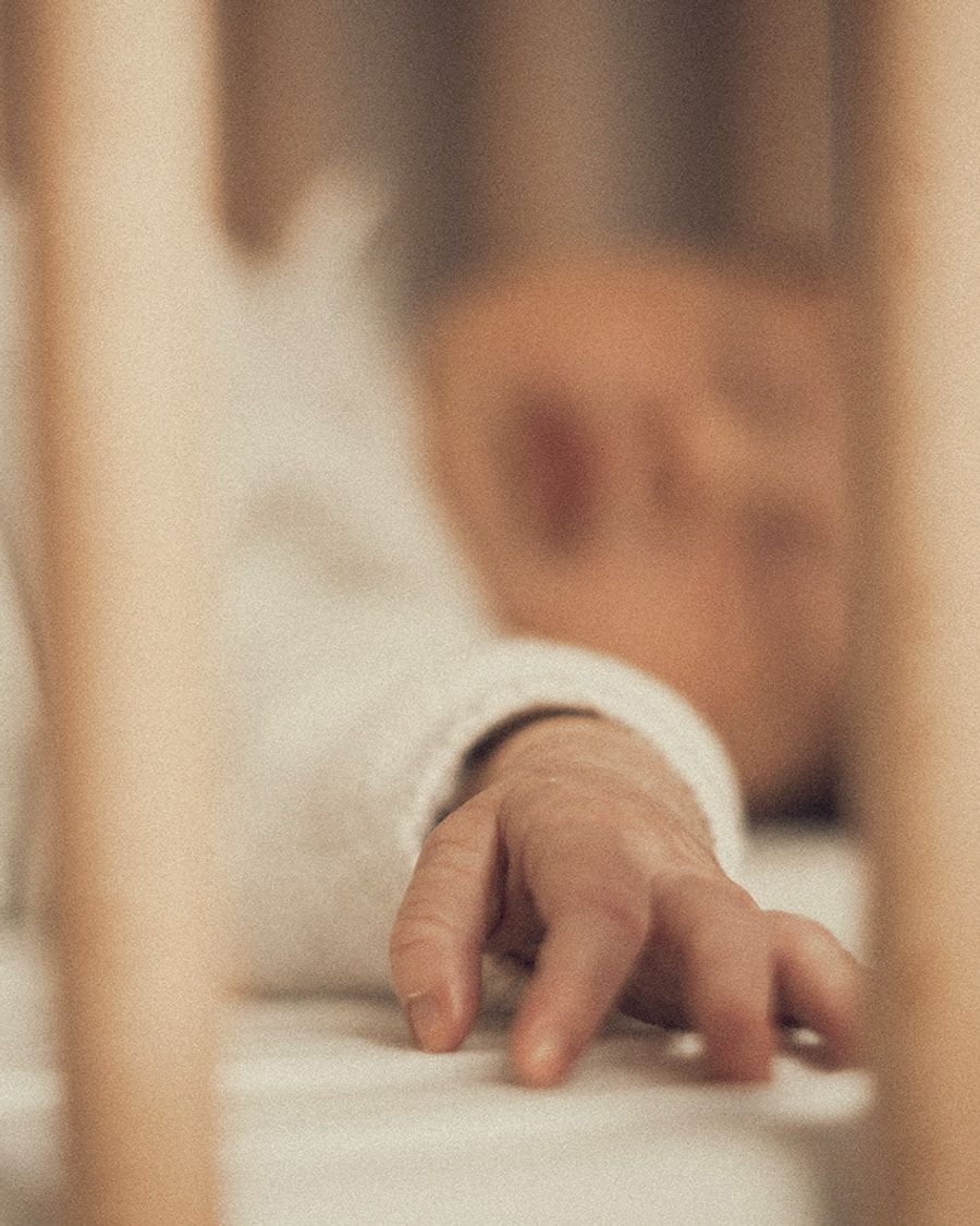 La main d’un bébé tendue entre les barreaux de son lit