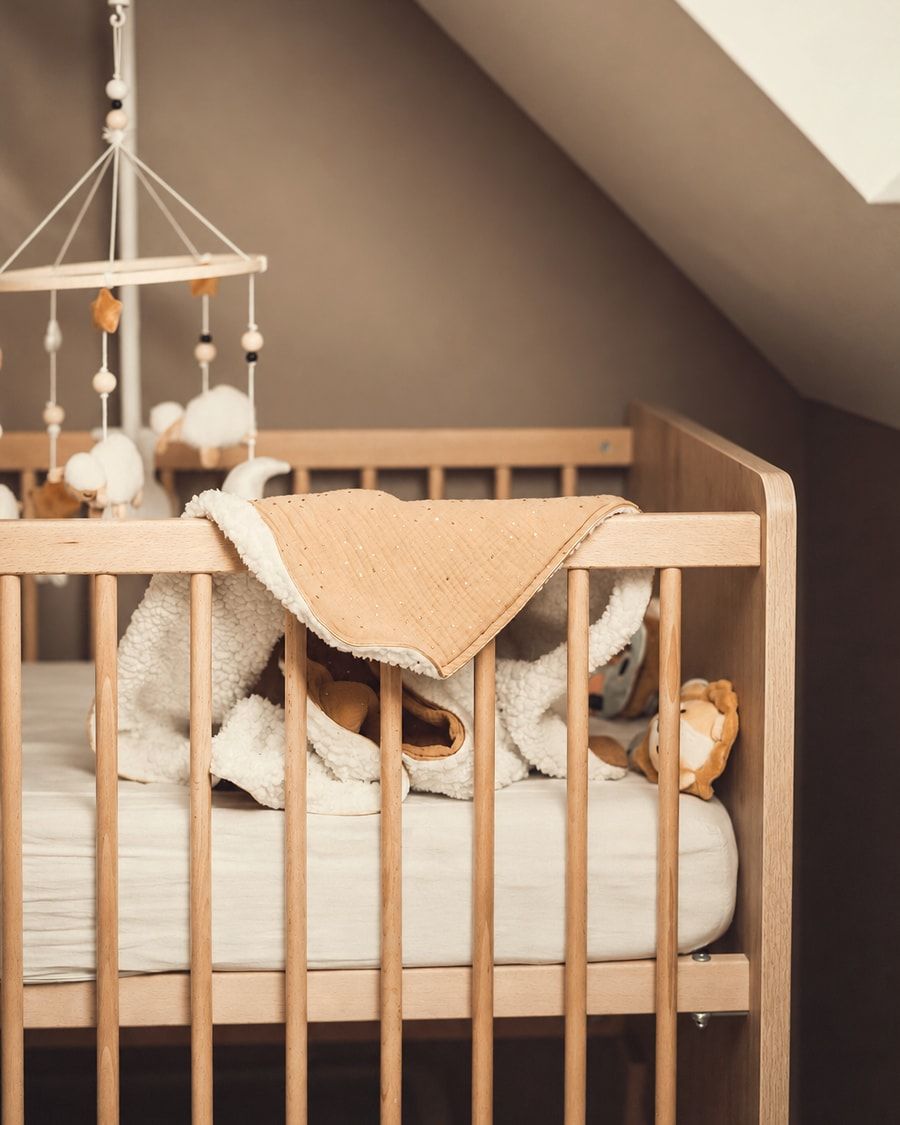 Un lit à barreaux en bois clair, une couverture posée sur le rebord, un mobile au-dessus